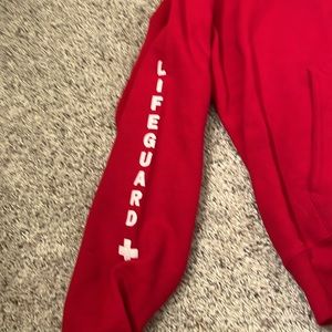 This sweatshirt is red and it says life guard on the front and on the side.